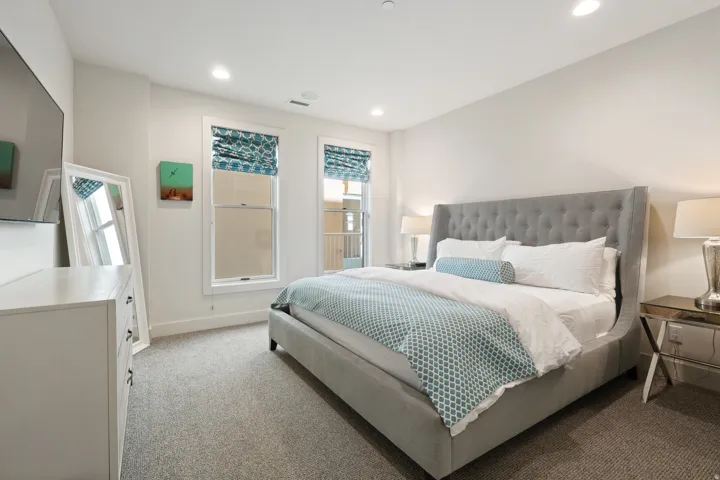Bedroom featuring light gray carpeting, two large windows with patterned Roman shades, recessed lighting, and a white baseboard trim
