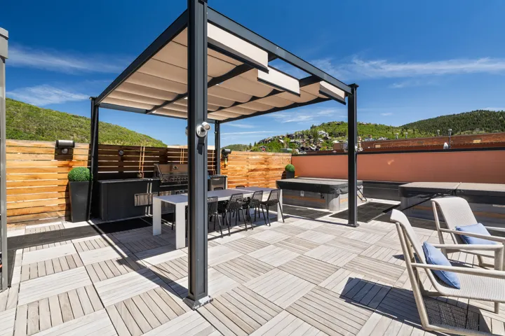 Expansive rooftop deck featuring a louvered pergola, wood-look flooring, two built-in hot tubs, a built-in outdoor grill station, and a wood slat privacy fence