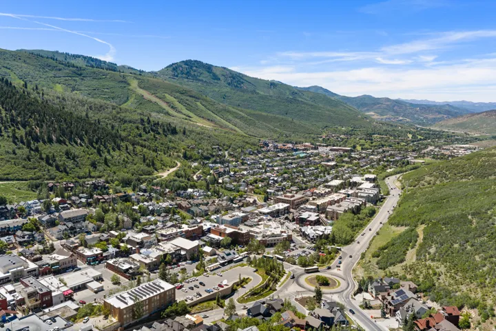 Aerial perspective showcasing a mountain town with extensive green hillsides, a central thoroughfare, a prominent roundabout, and a mix of commercial and residential structures