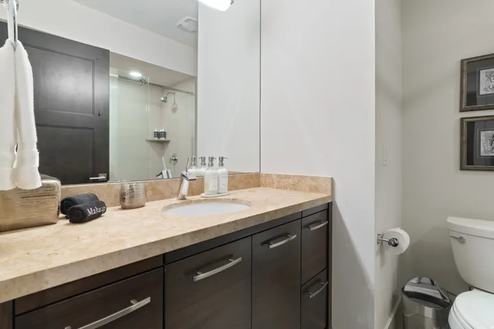 Contemporary bathroom featuring a dark wood-finish vanity with ample storage, a light-toned stone countertop, and an undermount sink