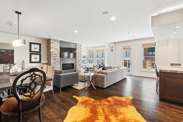 Spacious living area featuring rich wood-finish flooring, a contemporary fireplace with a stone surround, and multiple windows providing ample natural light