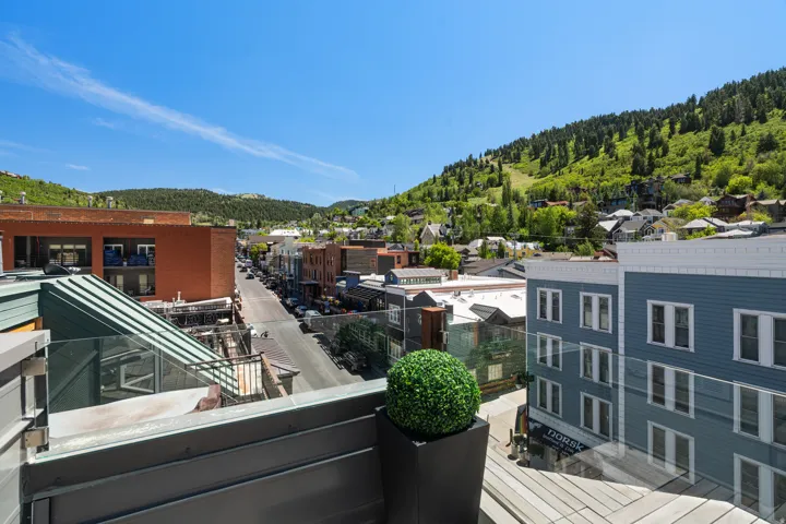 Rooftop terrace with glass panel railing overlooking a vibrant streetscape and distant tree-covered mountains