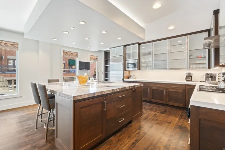 Expansive kitchen featuring a large central island with seating, rich wood cabinetry, white stone countertops, and glass-front upper cabinets