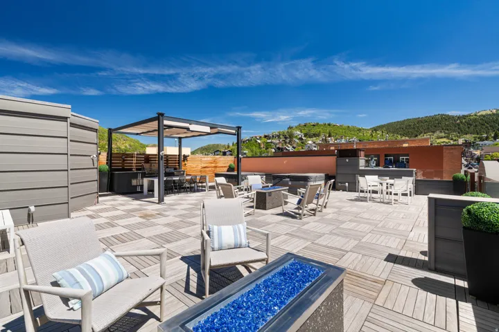 Expansive rooftop deck featuring modular wood-finish flooring, a built-in outdoor kitchen with a pergola, a gas fire pit, and partial mountain scenery