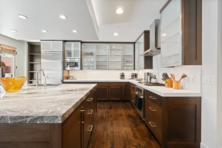 Gourmet kitchen featuring a substantial island with stone countertops, rich wood-finish cabinetry, stainless steel appliances, and wood-finish flooring