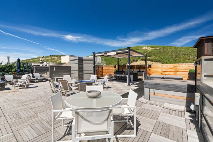 Expansive rooftop patio featuring wood-finish flooring, a built-in outdoor kitchen with a pergola, and a visible hot tub