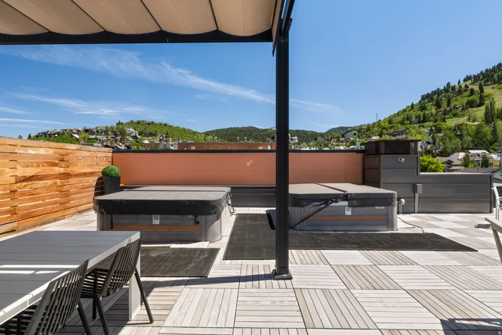 Rooftop deck featuring two built-in hot tubs, slatted wood privacy fencing, and a retractable awning