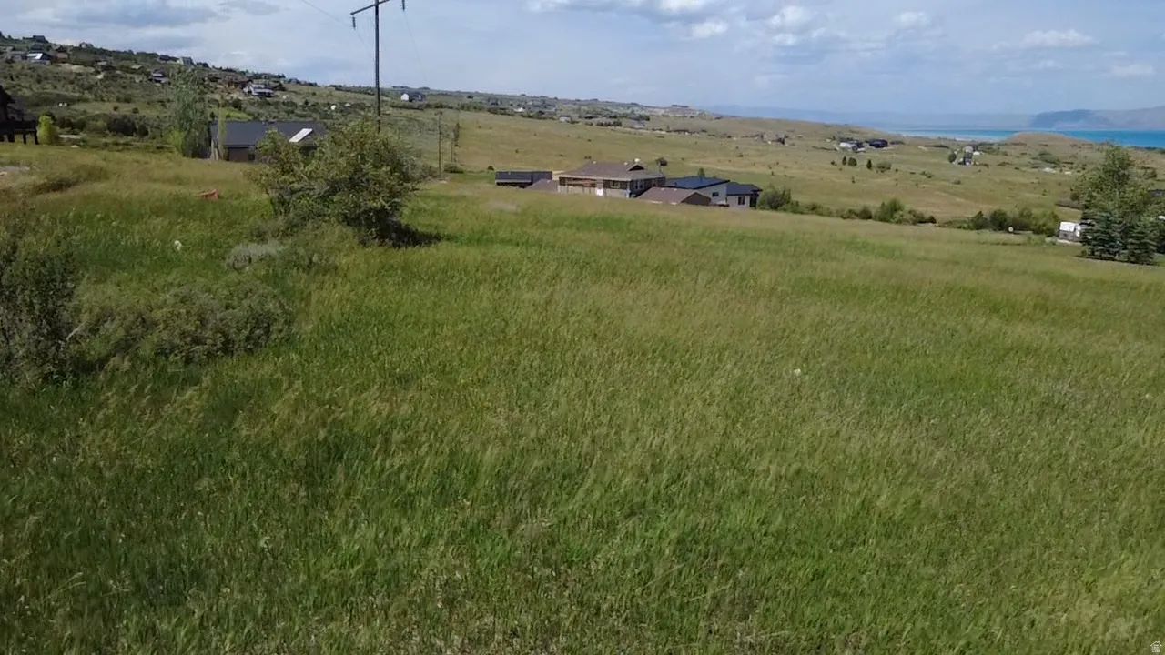 Expansive green field featuring varied topography with distant residential properties and a body of water under a partly cloudy sky