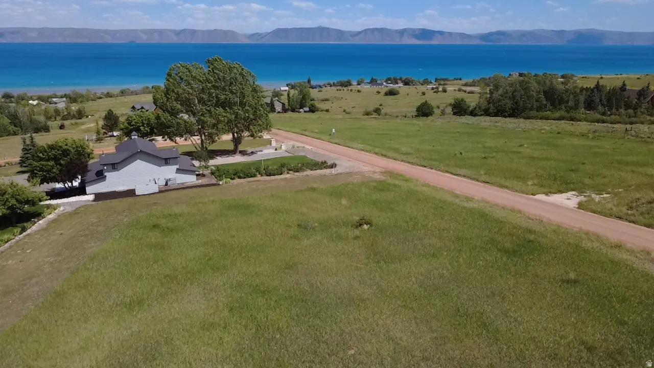 Expansive property featuring a modern gray residence with a dark roofline, set against a backdrop of a large body of water and distant mountains