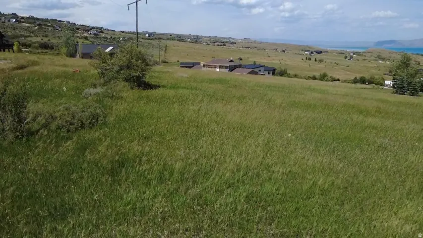 Expansive green field featuring varied topography with distant residential properties and a body of water under a partly cloudy sky