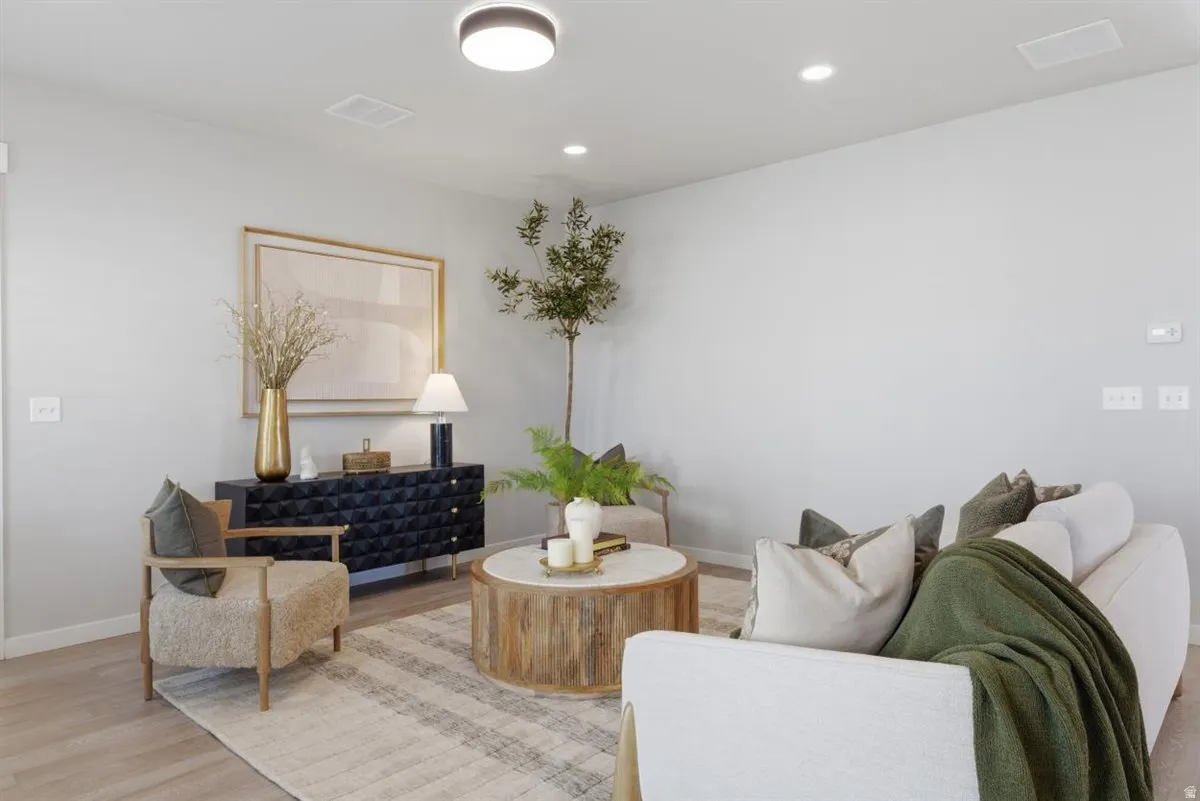 Spacious living area featuring light wood-finish flooring, a contemporary ceiling light fixture, recessed lighting, and crisp white walls