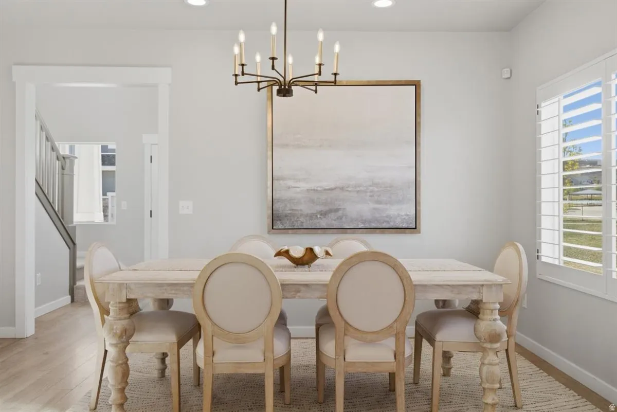 Open-concept dining area featuring a candelabra-style chandelier, plank flooring, and a large window with plantation shutters