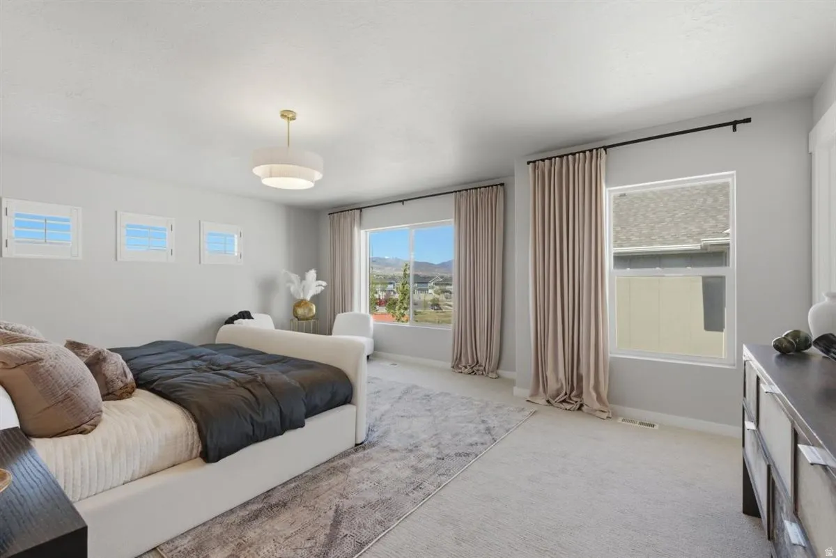 Spacious bedroom featuring light gray walls, plush carpeting, a modern ceiling fixture, multiple windows, and a large window overlooking a distant landscape