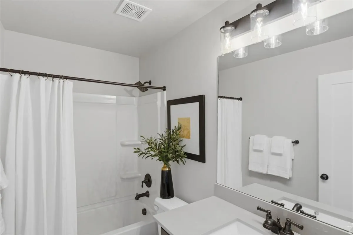 Bathroom featuring a white tub/shower combination with dark bronze fixtures, a vanity with a light countertop, integrated sink, and dark bronze faucet, and a large wall-mounted mirror