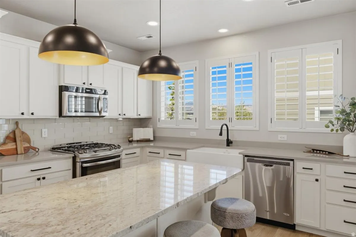 Modern kitchen featuring a large island with stone countertops, white shaker cabinetry, stainless steel appliances, and a subway tile backsplash
