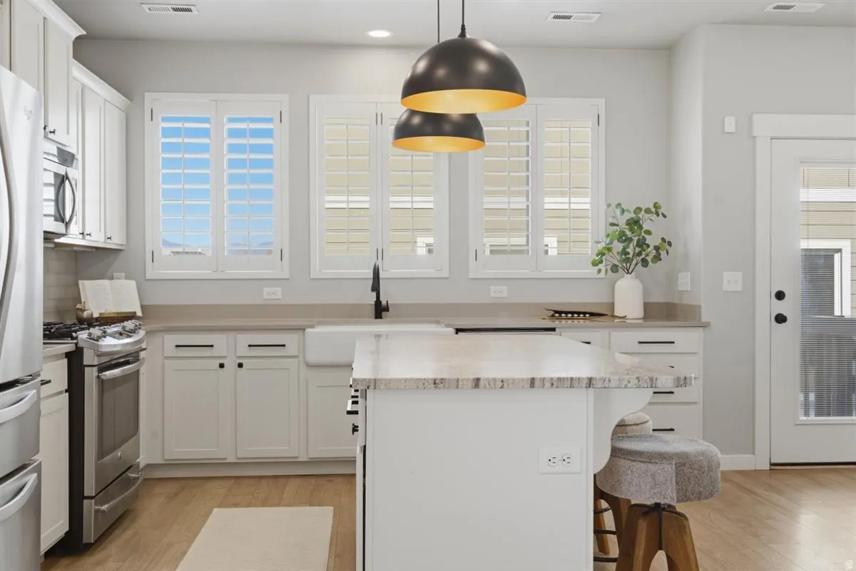 Modern kitchen featuring an island with stone countertops, a farmhouse sink, stainless steel appliances, and white cabinetry with dark hardware