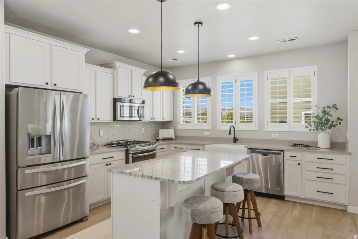 Bright kitchen featuring white shaker cabinetry, stainless steel appliances, a large central island with seating, pendant lighting, and light wood-finish flooring