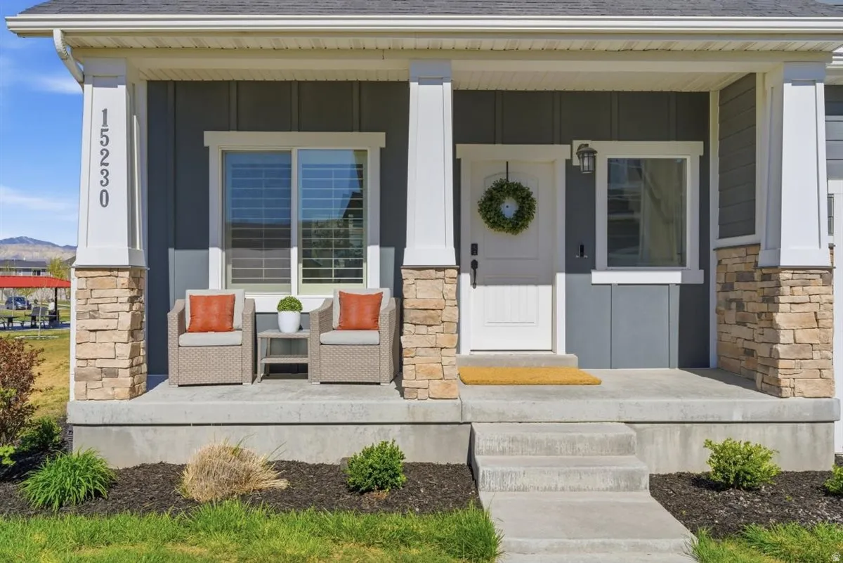 Inviting front porch featuring stone-clad pillars, a white paneled entry door, and a built-in exterior light fixture