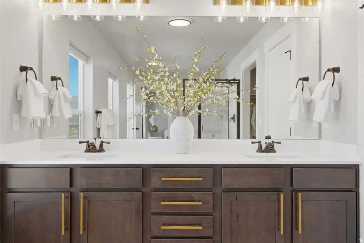 Dual vanity featuring dark wood-finish cabinetry with gold-tone hardware, white countertops, and bronze-tone faucets