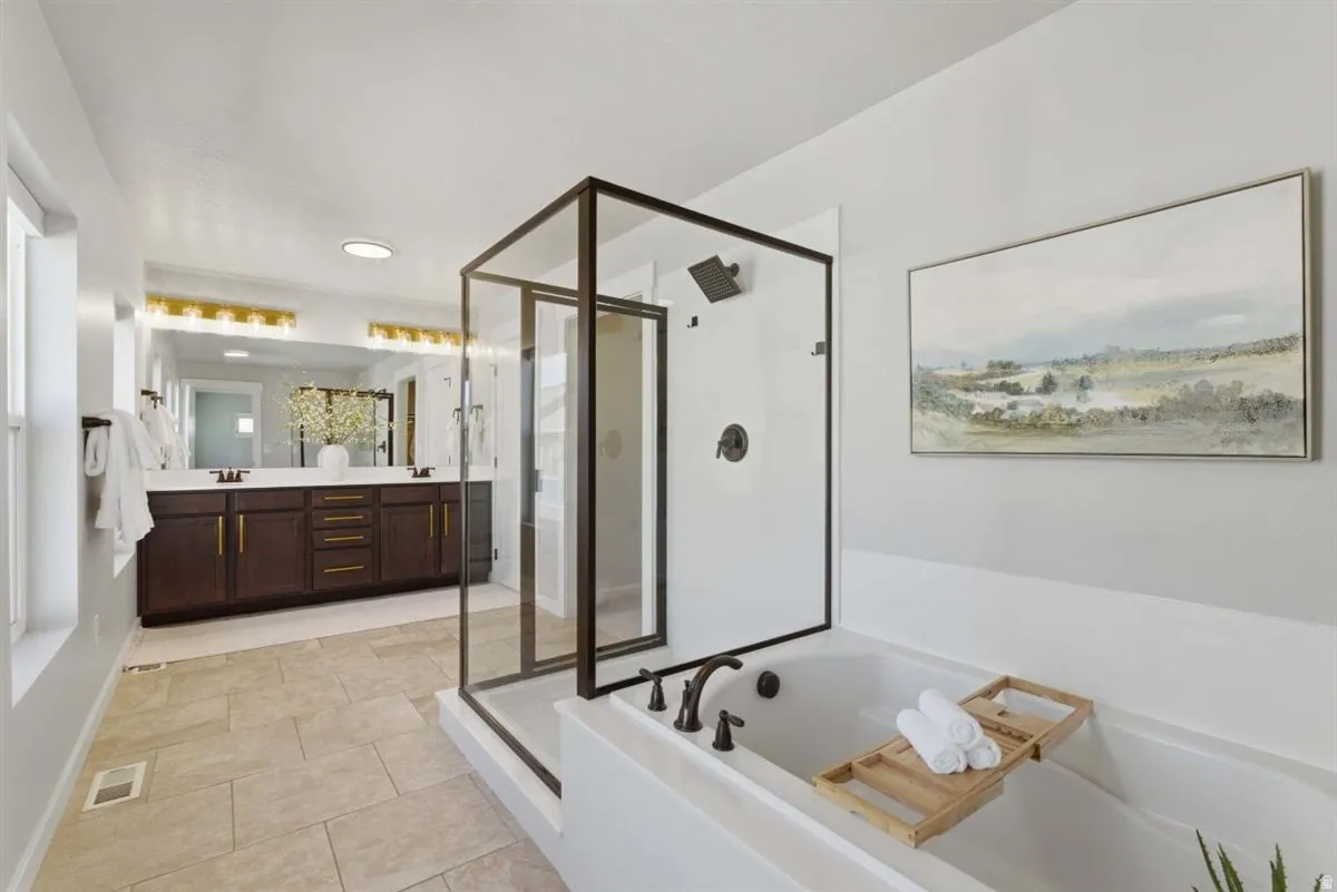 Bathroom featuring a large soaking tub, glass-enclosed shower with a rainfall showerhead, and a double vanity with dark wood cabinetry and gold-toned hardware