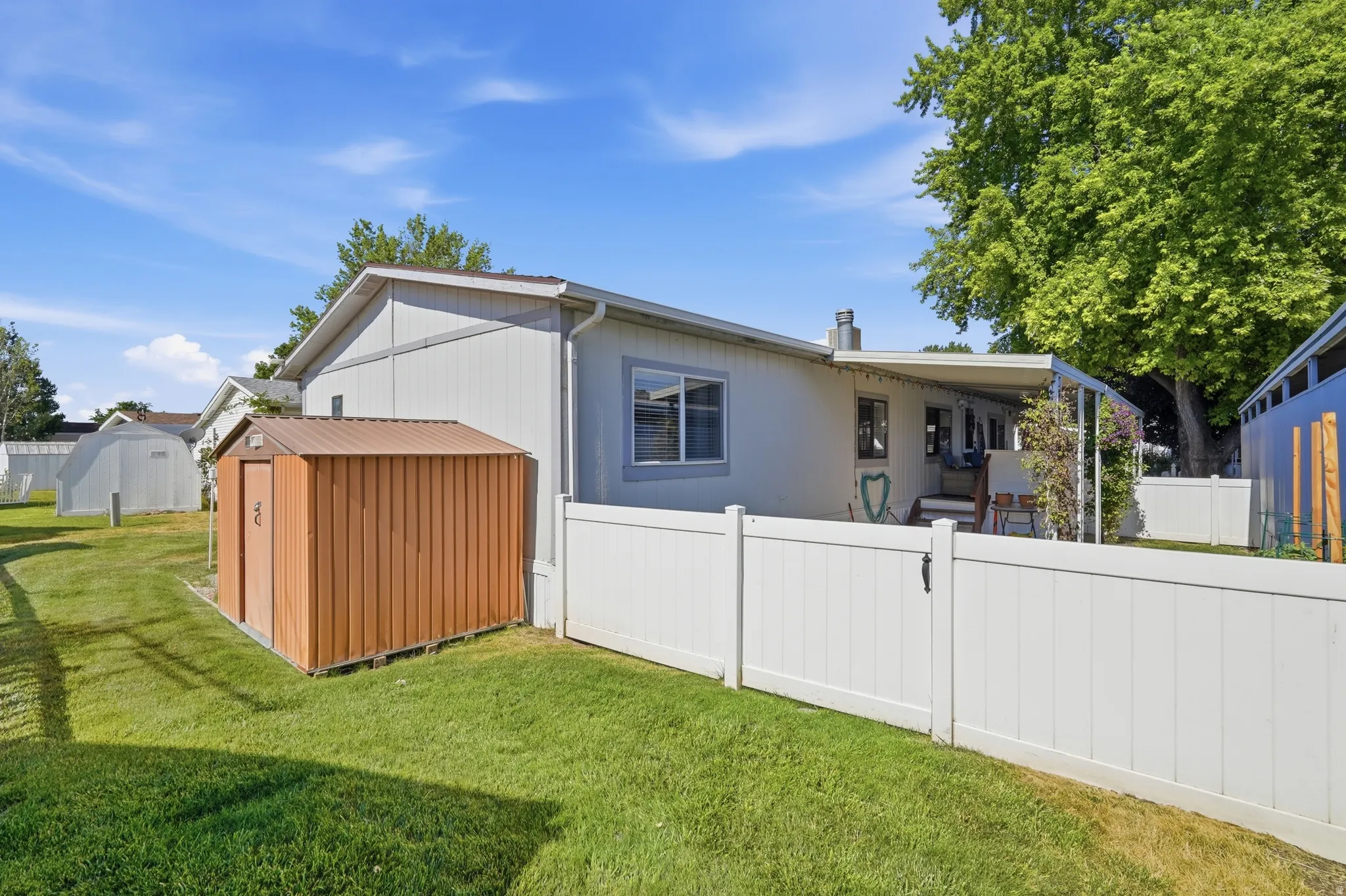 Spacious green lawn with a brown metal storage shed, white privacy fencing, and a covered back patio