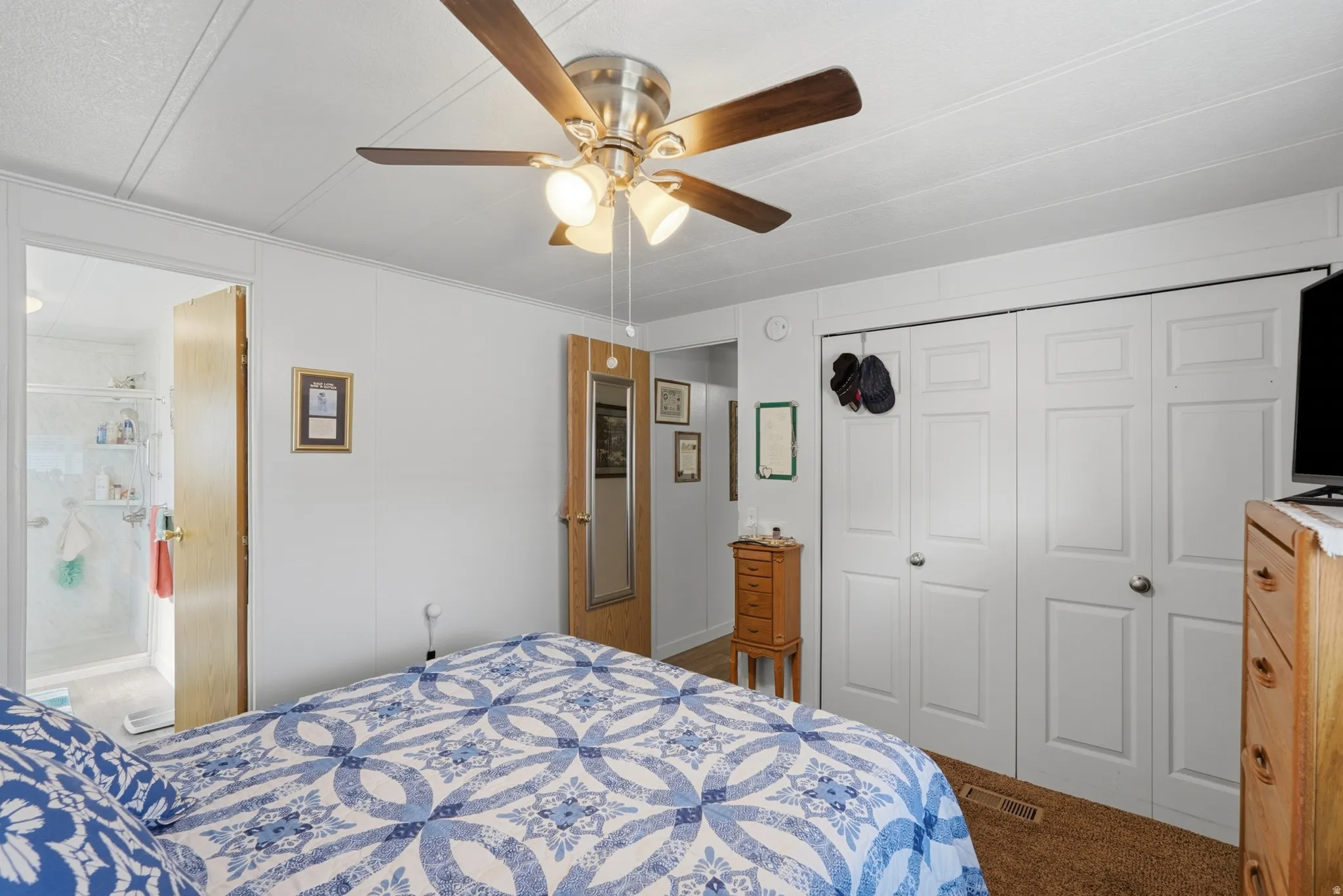 Bedroom featuring a ceiling fan, white paneled walls, brown carpet flooring, and bi-fold closet doors