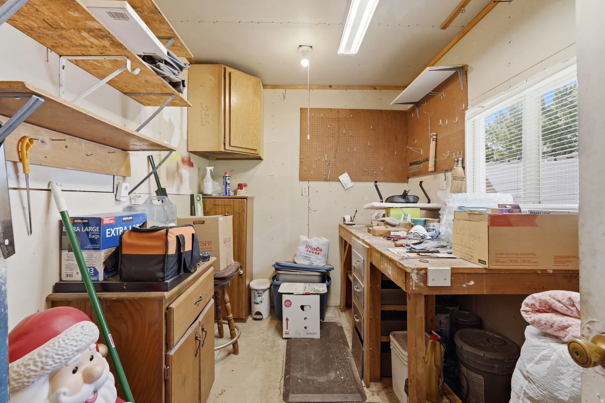 Utility room featuring built-in wooden shelving, a large workbench, upper and lower cabinetry, a pegboard wall, and a window with blinds