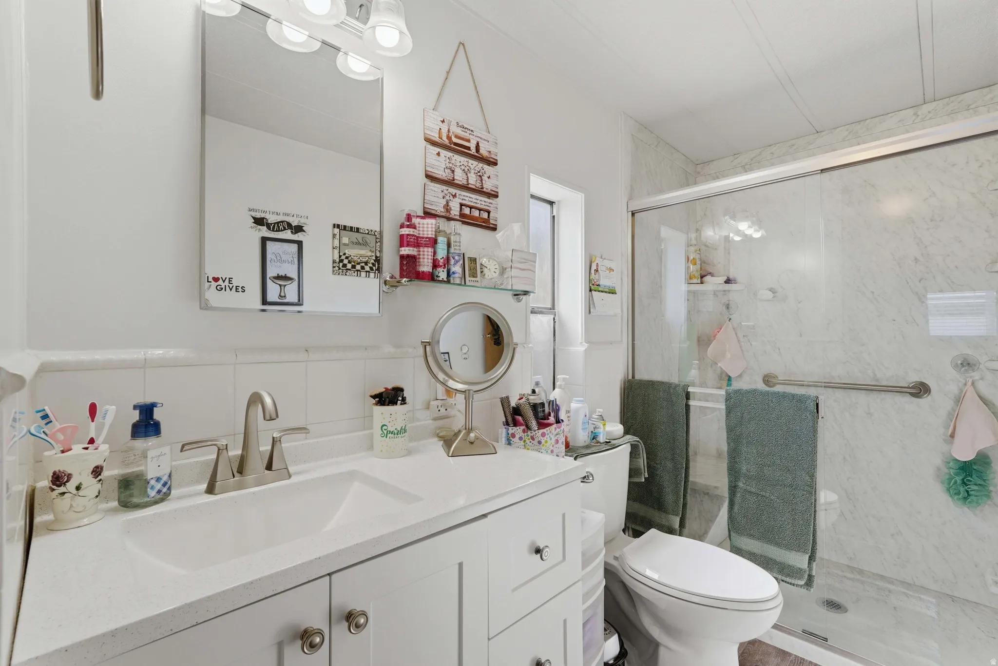 Bathroom featuring a white vanity with integrated sink, brushed nickel faucet, large wall mirror, and a glass-enclosed shower with marble-look wall panels