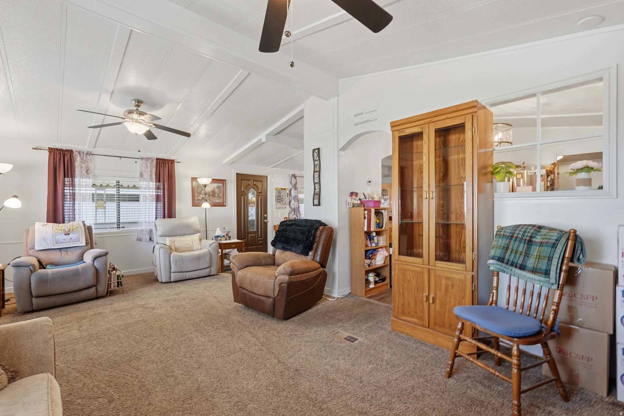 Spacious living area featuring vaulted ceilings with decorative paneling and dual ceiling fans