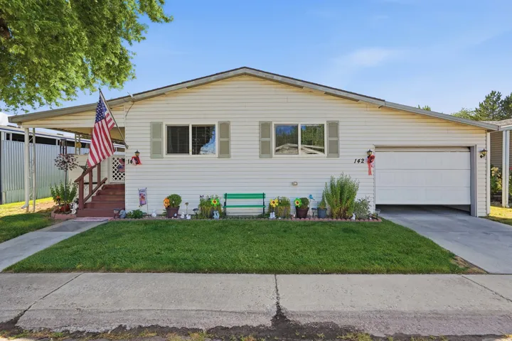 Single-story residence featuring white horizontal siding, a covered front porch with wooden steps, and a paved driveway leading to an attached garage