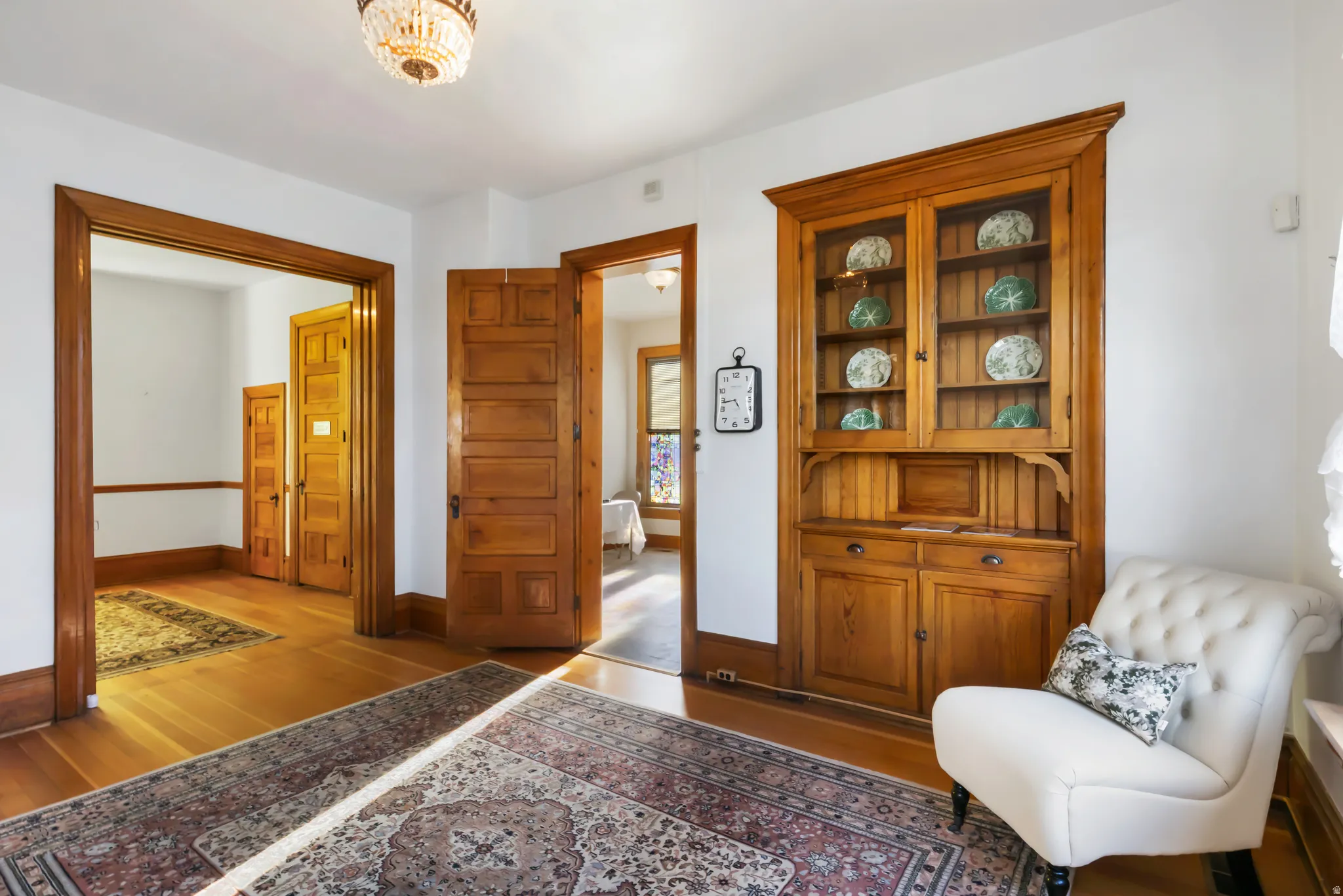Hardwood flooring throughout featuring a built-in wood display cabinet with glass doors, solid wood doors, and a decorative chandelier