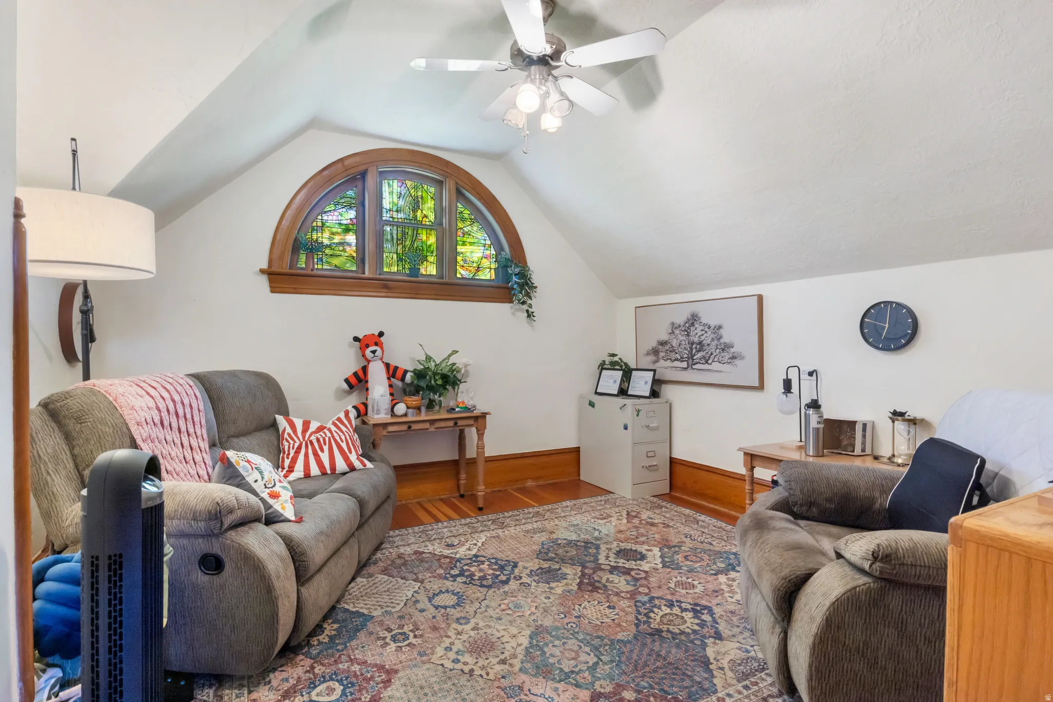 Attic space featuring a prominent arched window with wood trim, wood-finish flooring, and a ceiling fan with integrated lighting