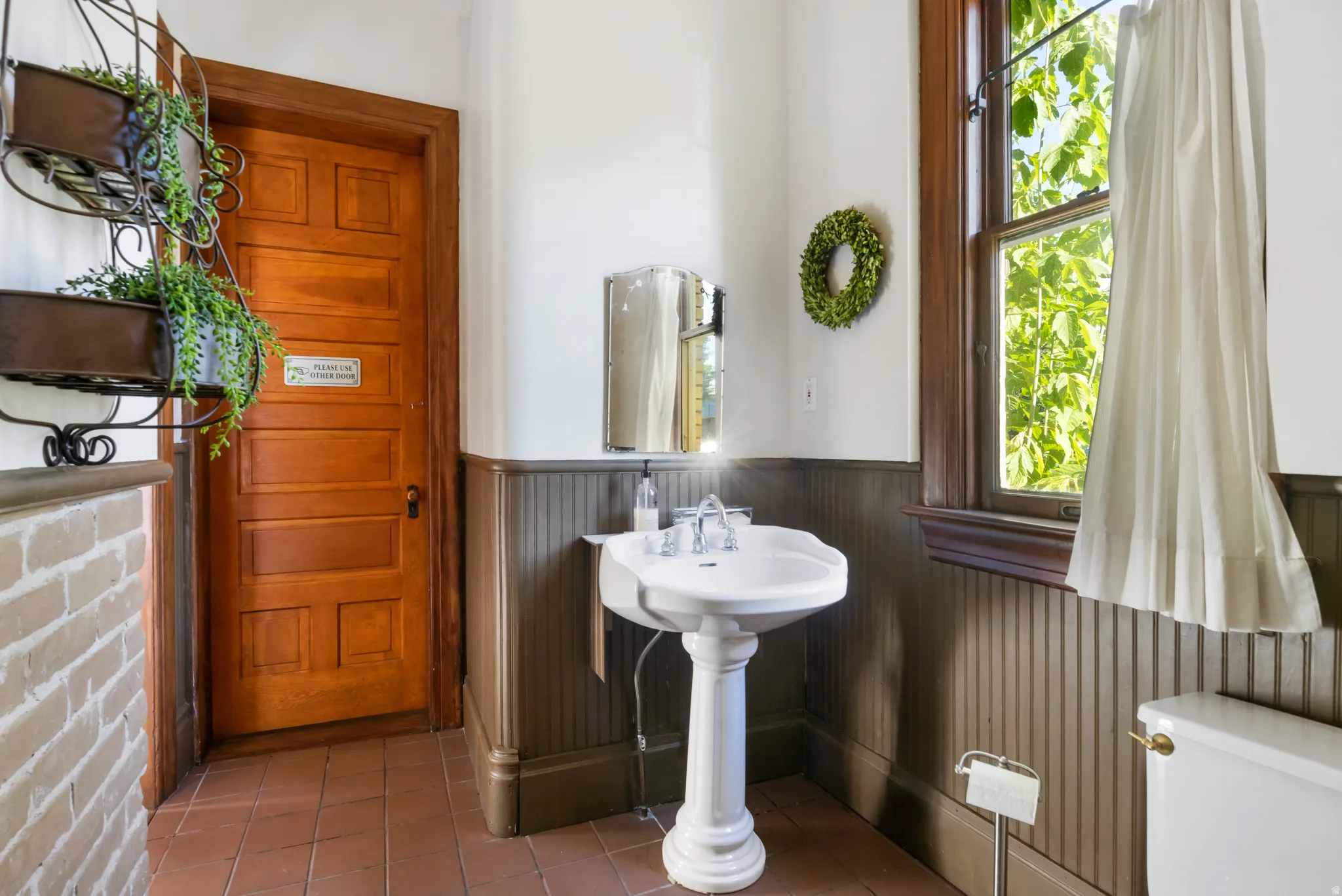 Pedestal sink with chrome fixtures, beadboard wainscoting, and wood-finish trim framing a window