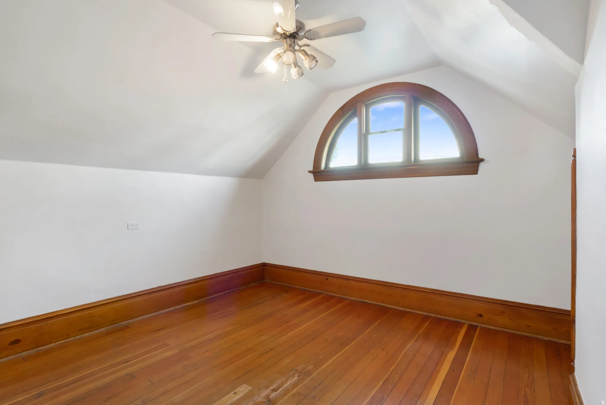 Room featuring an arched window with wood trim, wood-finish flooring, and white painted walls