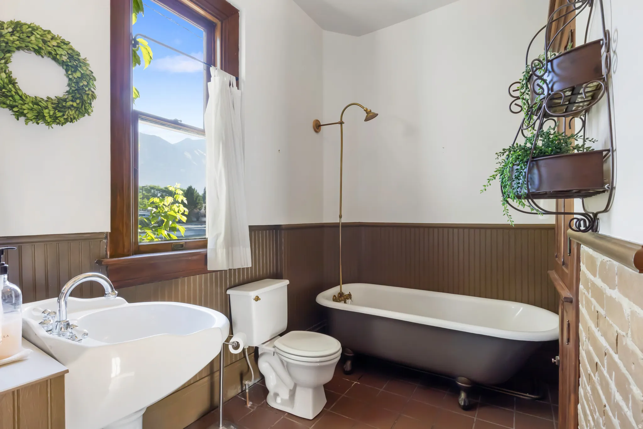 Bathroom featuring a classic clawfoot tub with a vintage-style shower fixture, a pedestal sink with chrome hardware, and terracotta-toned floor tiles