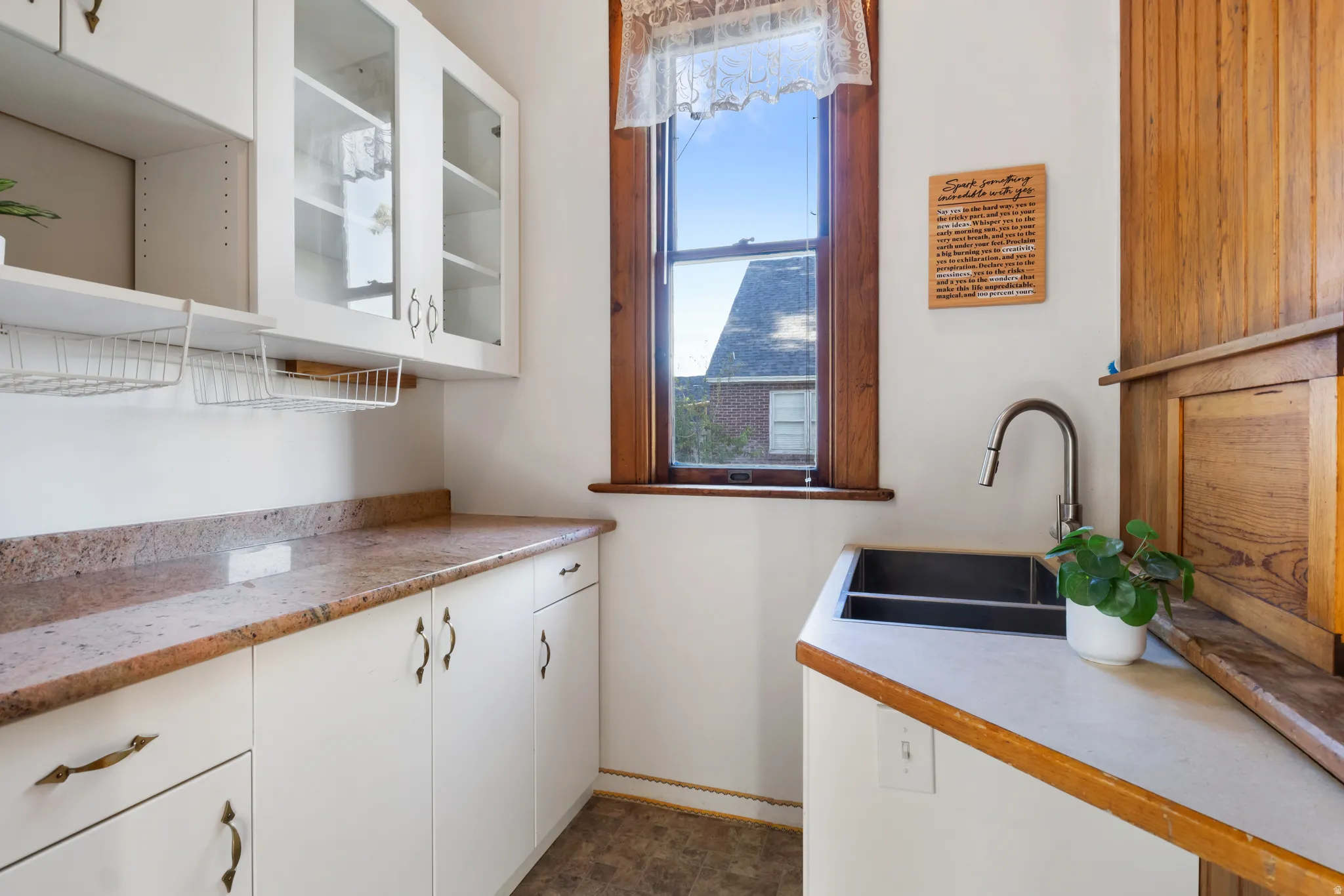 Kitchenette area featuring white cabinetry, a dual-basin sink with a gooseneck faucet, a wood-framed window, and stone-finish countertops