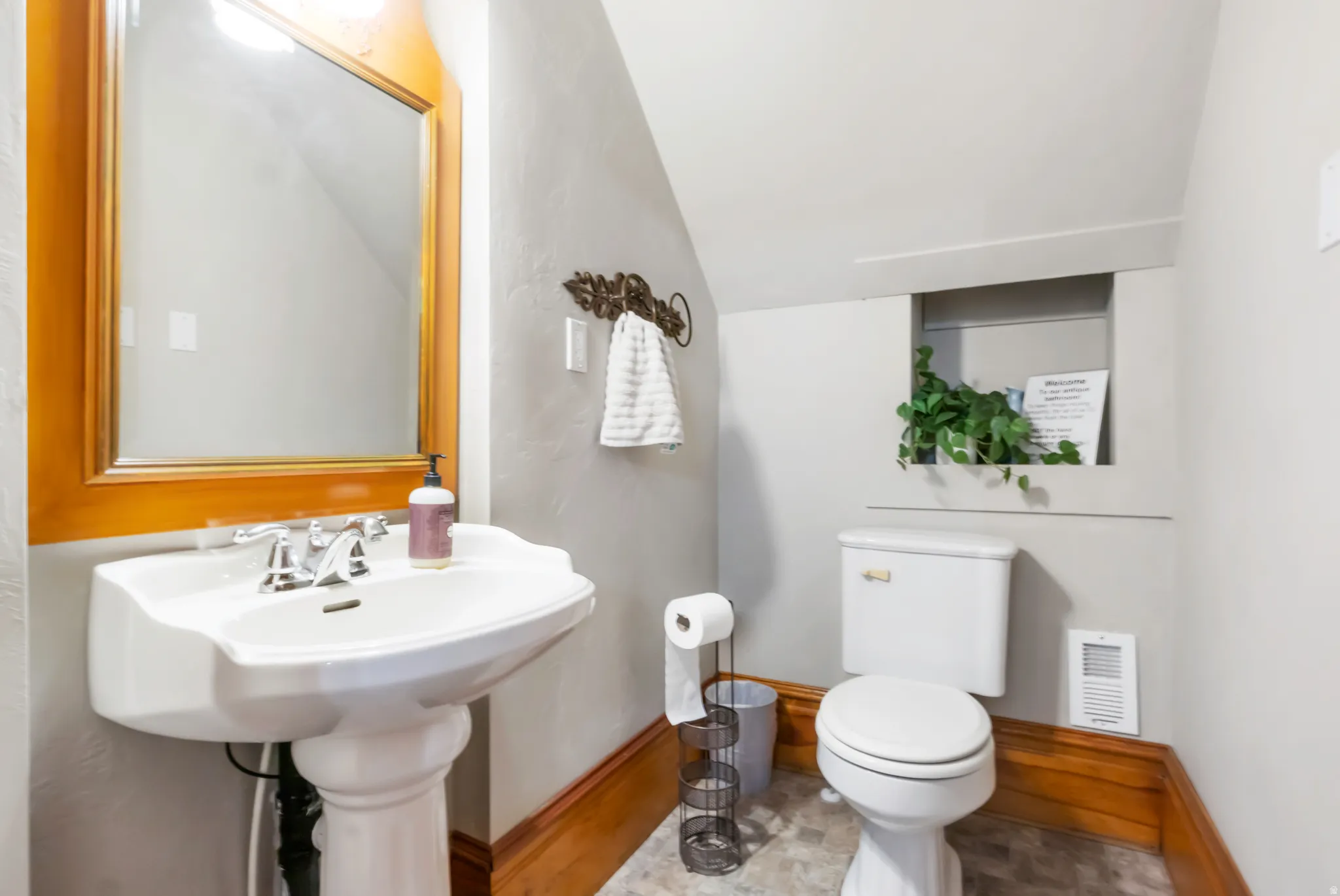 Bathroom featuring a white pedestal sink with chrome faucet, a framed wood mirror, white toilet, and recessed wall niche