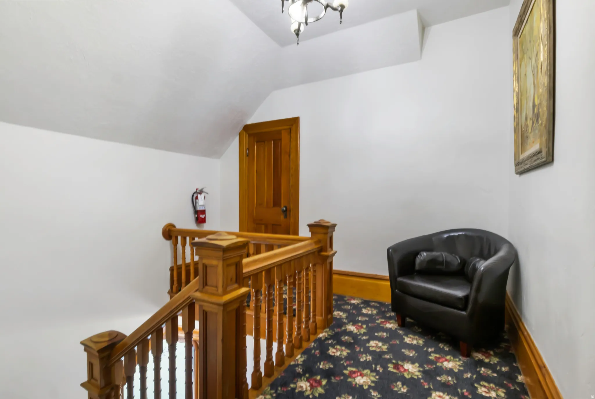Upper-level landing featuring polished wood banister and trim, a patterned carpet, and a wood-paneled door
