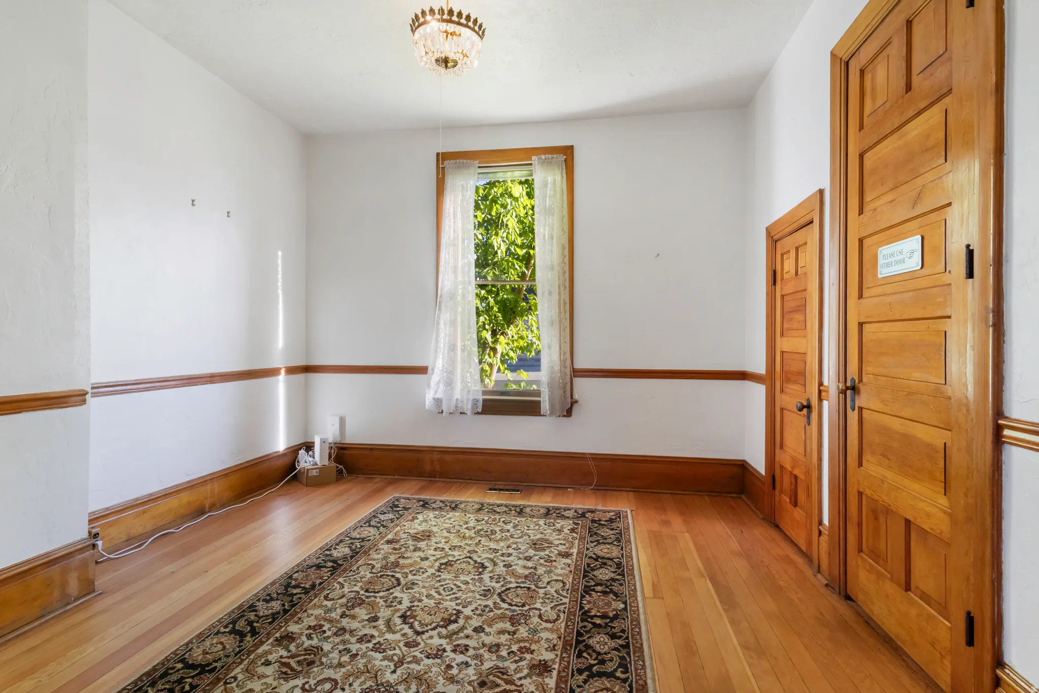 Hardwood flooring featuring an ornate area rug, white walls with wood trim, a window with exterior foliage, and two wood-paneled doors