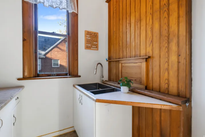 Compact kitchen area featuring a double basin stainless steel sink, wood-finish wall paneling, and white cabinetry with curved hardware
