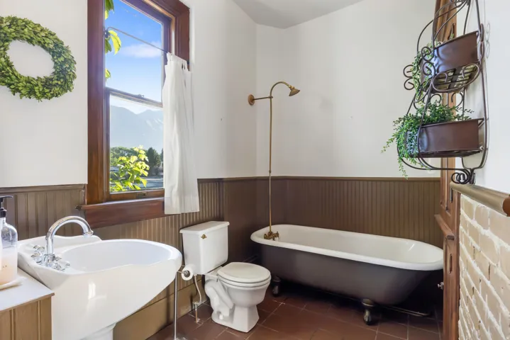 Bathroom featuring a classic clawfoot tub with a vintage-style shower fixture, a pedestal sink with chrome hardware, and terracotta-toned floor tiles