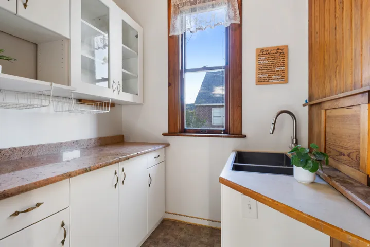 Kitchenette area featuring white cabinetry, a dual-basin sink with a gooseneck faucet, a wood-framed window, and stone-finish countertops