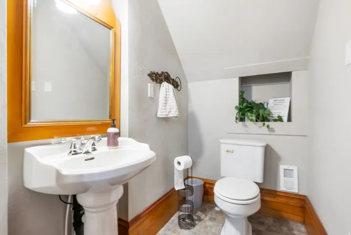 Bathroom featuring a white pedestal sink with chrome faucet, a framed wood mirror, white toilet, and recessed wall niche