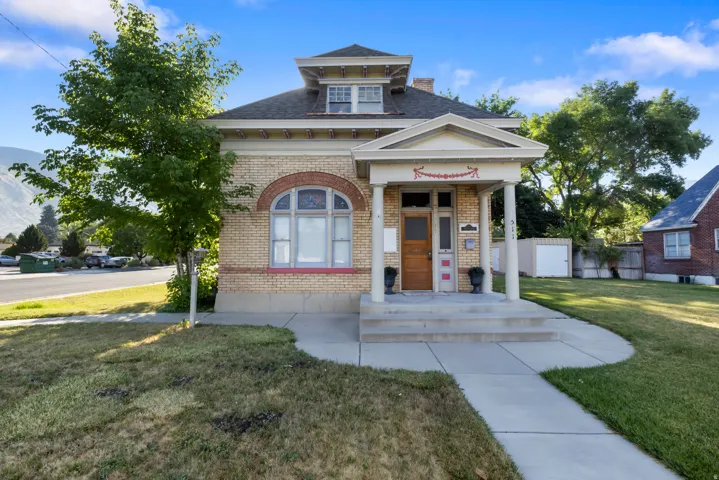 Brick facade home featuring a prominent portico with white columns, a pitched roofline, and an arched window with decorative glass