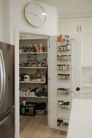 Walk-in pantry with multiple shelving units, door-mounted spice racks, and wood-finish flooring