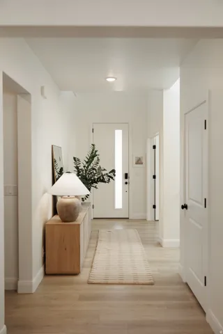 Bright hallway featuring light wood-finish flooring, recessed lighting, and a white entry door with a vertical frosted glass insert