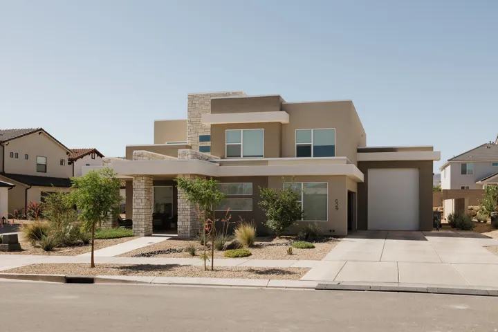 Modern stucco exterior with stone accents, a concrete driveway, a front walkway, an integrated garage, and low-maintenance landscaping