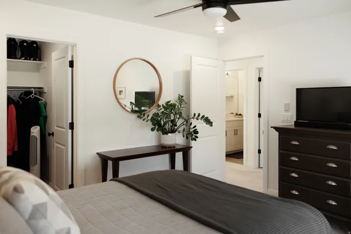 Bedroom featuring a ceiling fan with integrated lighting, a closet with shelving and hanging space, and an en-suite bathroom entry with vanity visible