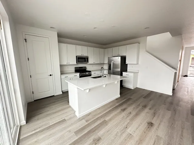 Kitchen featuring an island with a built-in sink, stainless steel appliances, white cabinetry, and wood-finish flooring