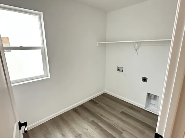 Dedicated utility space featuring a single-pane window, wood-finish flooring, white walls, and a built-in wall shelf